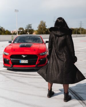 Czarny kożuch damski z kapturem, długim krojem i futrzanym wykończeniem, idealny na zimowe dni