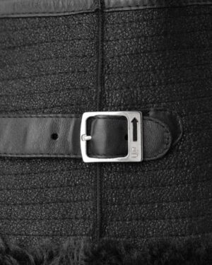 Czarny kożuch damski z futrzanym wykończeniem, ozdobiony skórzanym paskiem z metalową klamrą